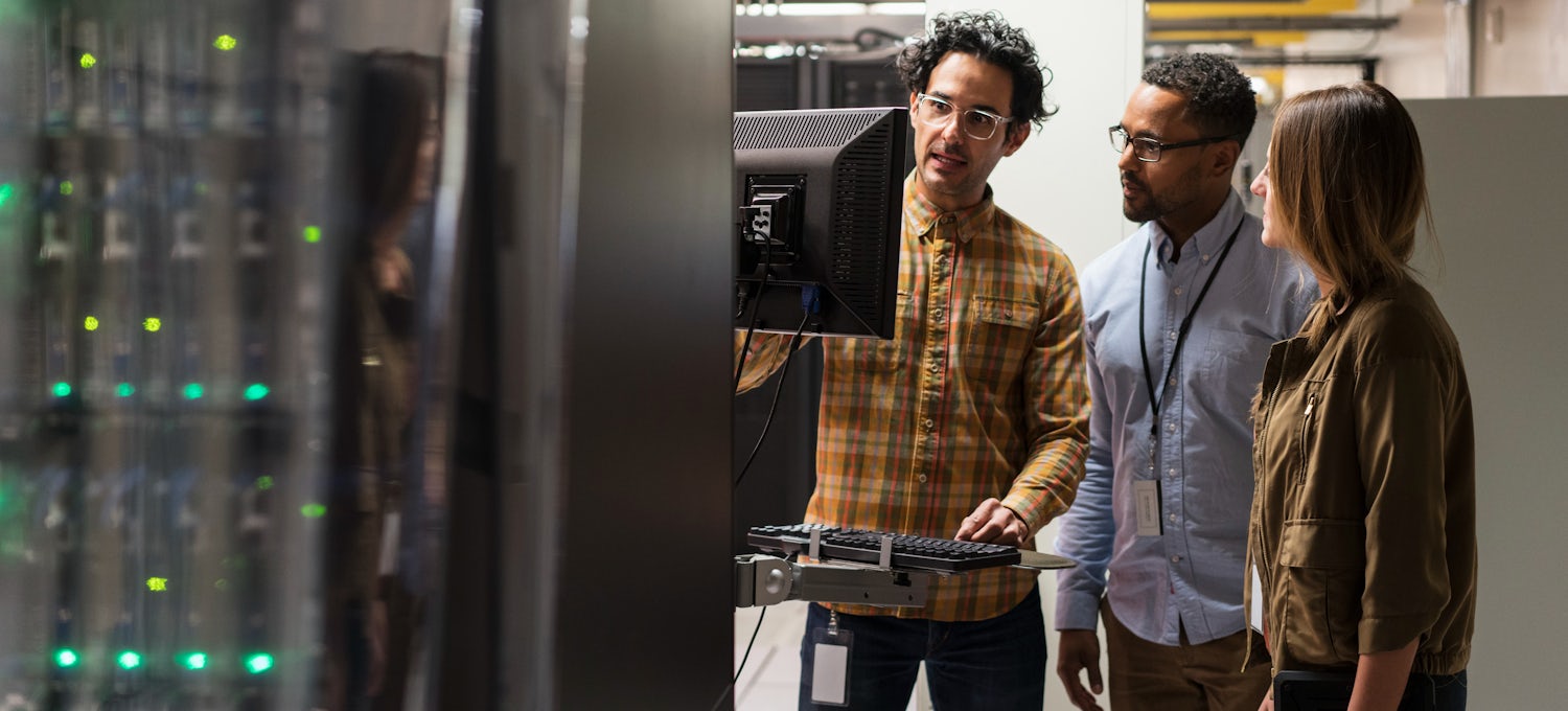 [Featured image] Three AI engineers look at a monitor in a data server room.