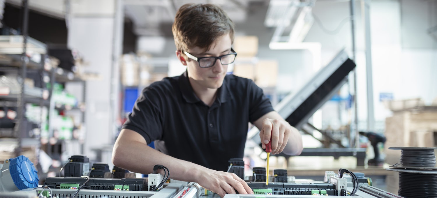 [Featured image] A young white man with glasses works on a circuit board.
