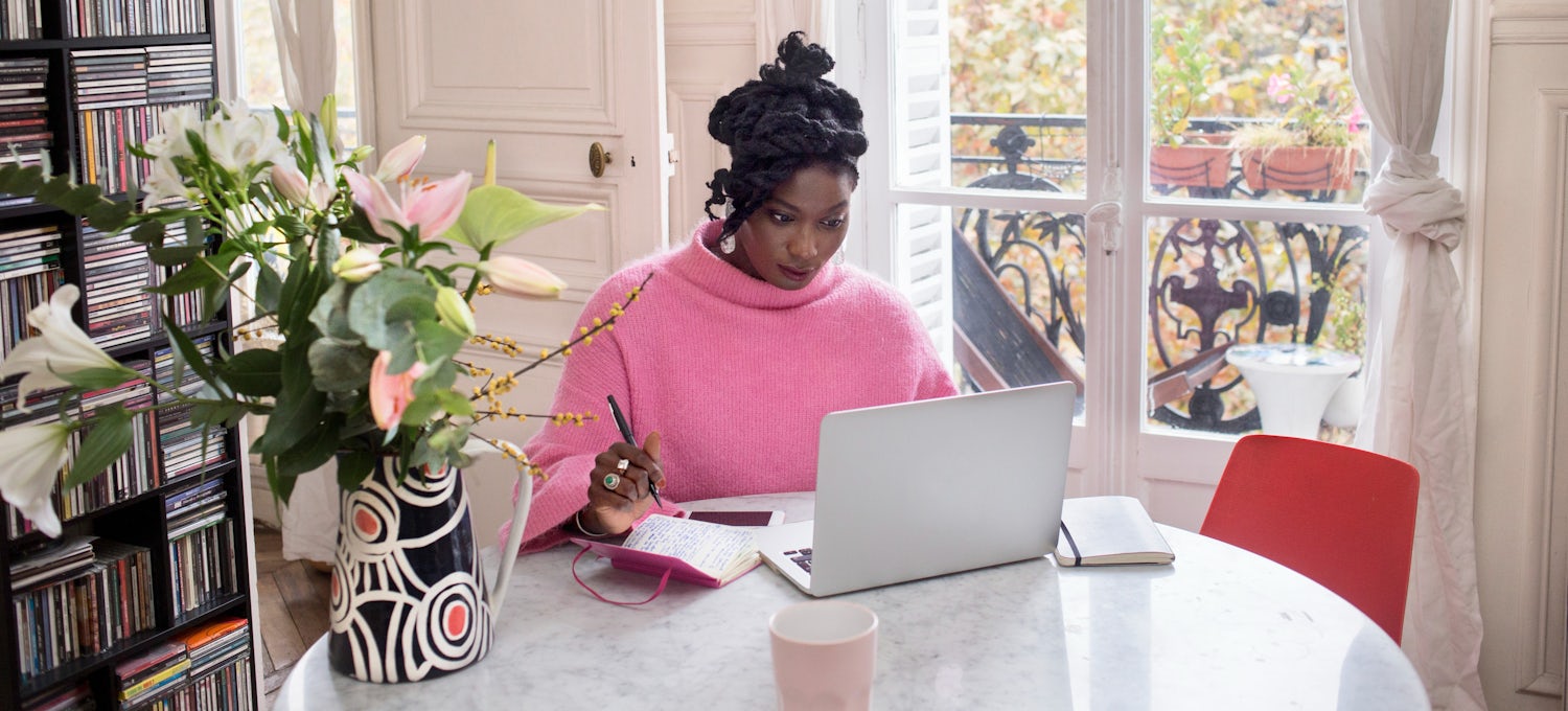 A woman works on her Google Ads campaign on a laptop while sitting at a table by a window.