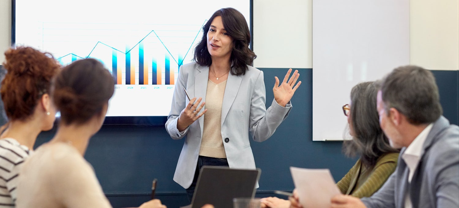 [Imagen destacada] Una mujer con traje de negocios presenta una estrategia de comercialización a su equipo en una sala de conferencias.