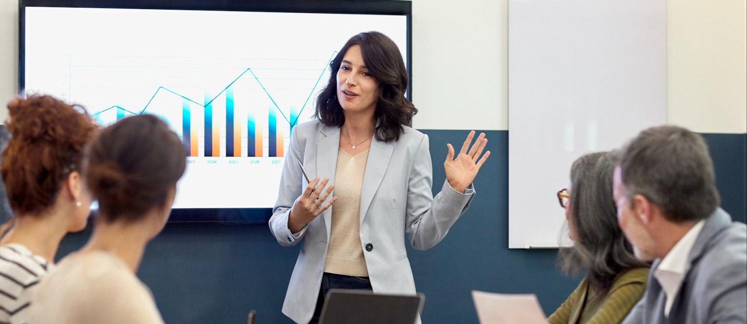 [Featured image] A woman stands in front of a screen presenting marketing analytics to stakeholders.