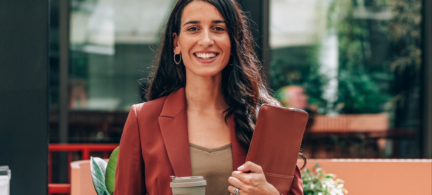[Featured image] A social worker holding a case file and a cup of coffee smiles at the camera.