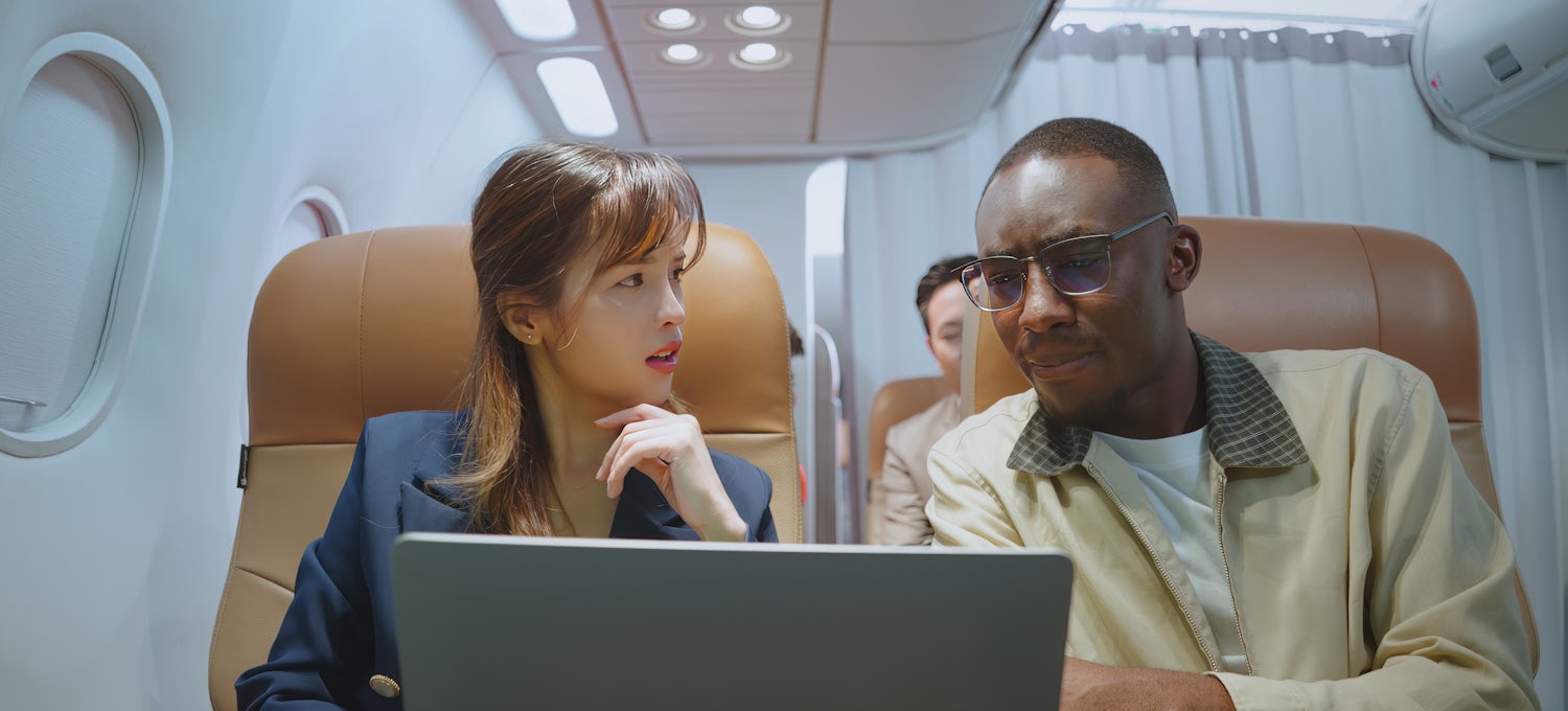[Featured Image] Two colleagues look at a laptop and discuss GDPR while sitting on a plane, traveling to Europe. 