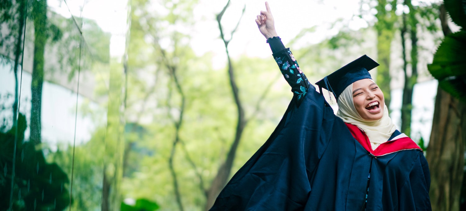 [Imagen destacada] Una joven con hiyab y vestido de graduación levanta el dedo en el aire. 