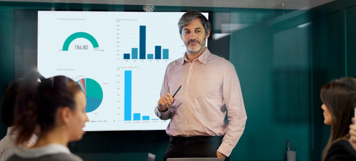 [Featured image] Man showing group graphs of product performance on a projection screen