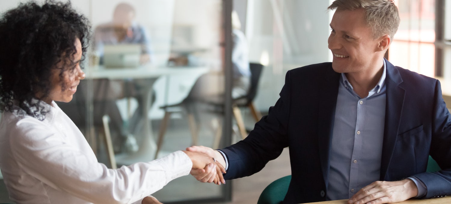 [Featured image] A tech salesperson shaking hands with a client in an office after just closing a deal.
