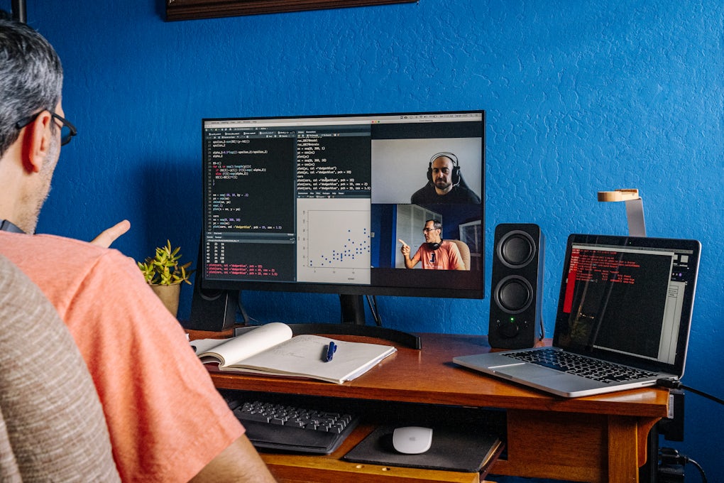 [Featured Image] A programmer examines code while on a video call with other members of his coding team.