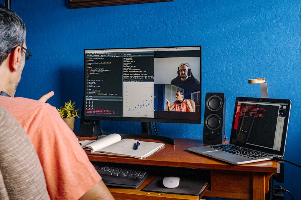 [Featured Image] A programmer examines code while on a video call with other members of his coding team.