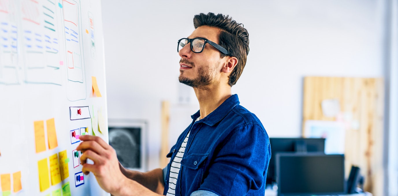 Male UX designer in glasses and a blue shirt drawing a wireframe on a whiteboard