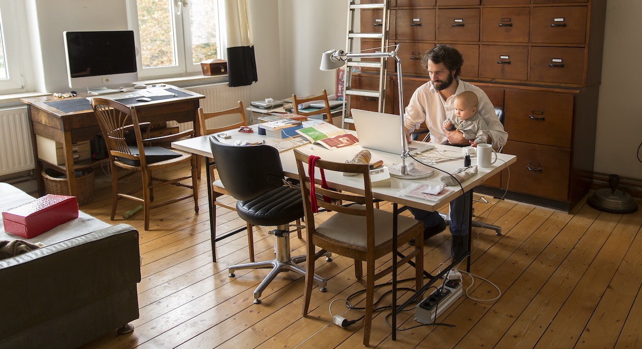 [Featured image] Employee working from home holding a baby as they types on their laptop