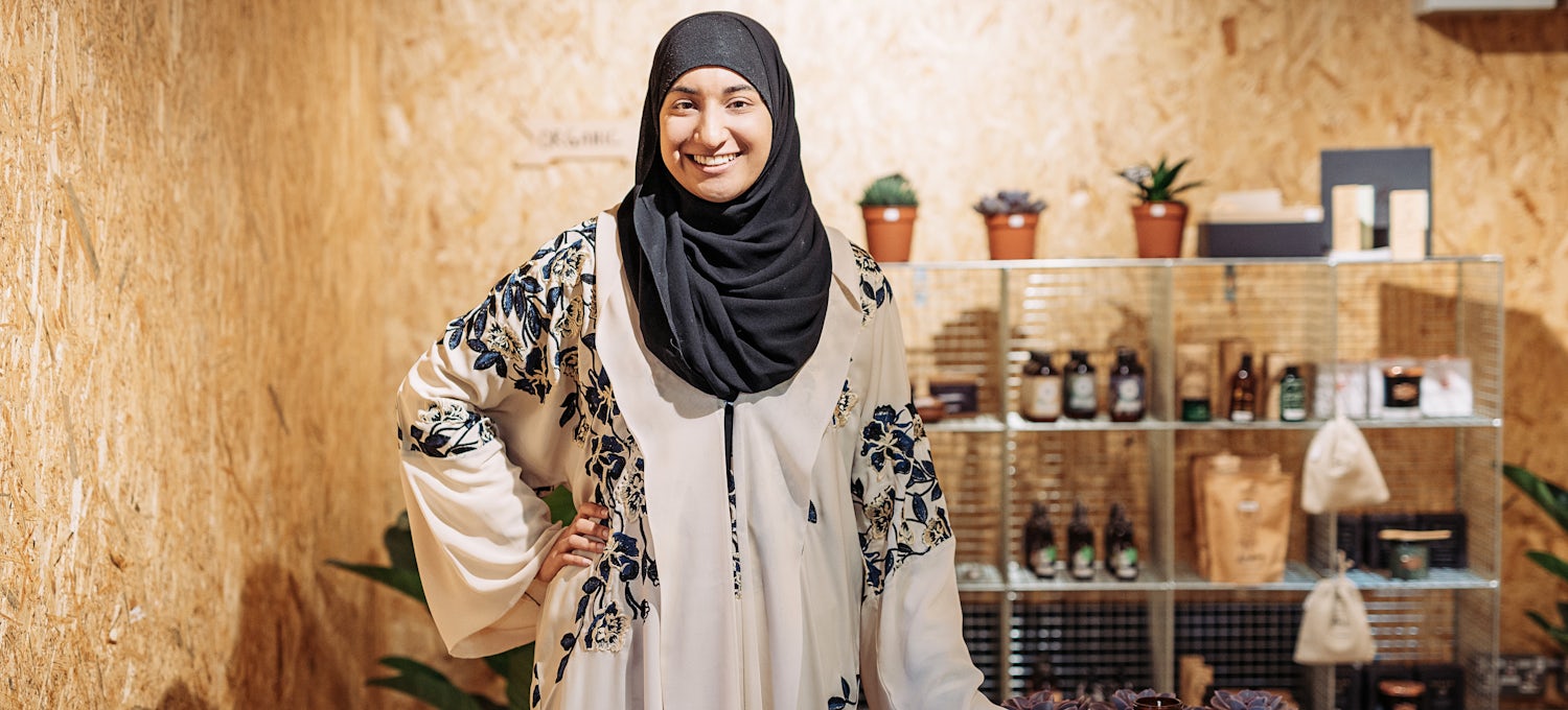 [Featured image] The owner of an apothecary small business stands in front of her products, smiling at the camera.