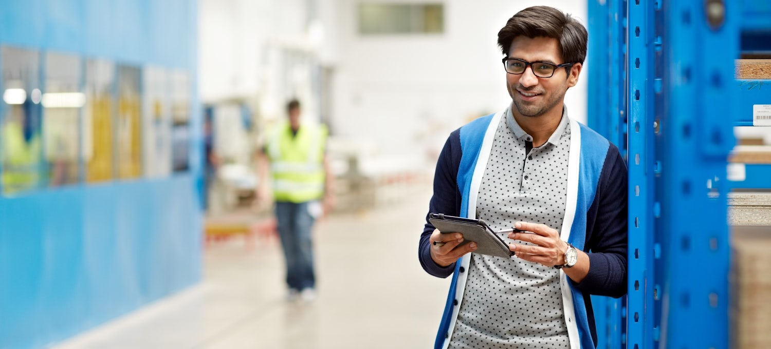 [Featured Image] A supply chain manager stands in a warehouse holding a tablet.