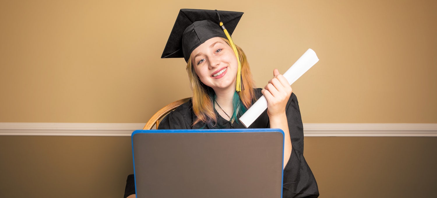 [Featured image] Data Analytics Master's Degree graduate in cap and gown sitting at a laptop