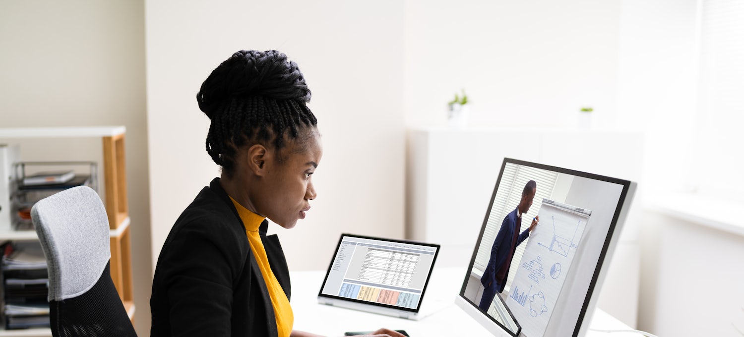 [Featured image] A female, wearing a dark jacket and orange top, is sitting in front of her desktop, connecting with a potential customer as an inside sales representative. 