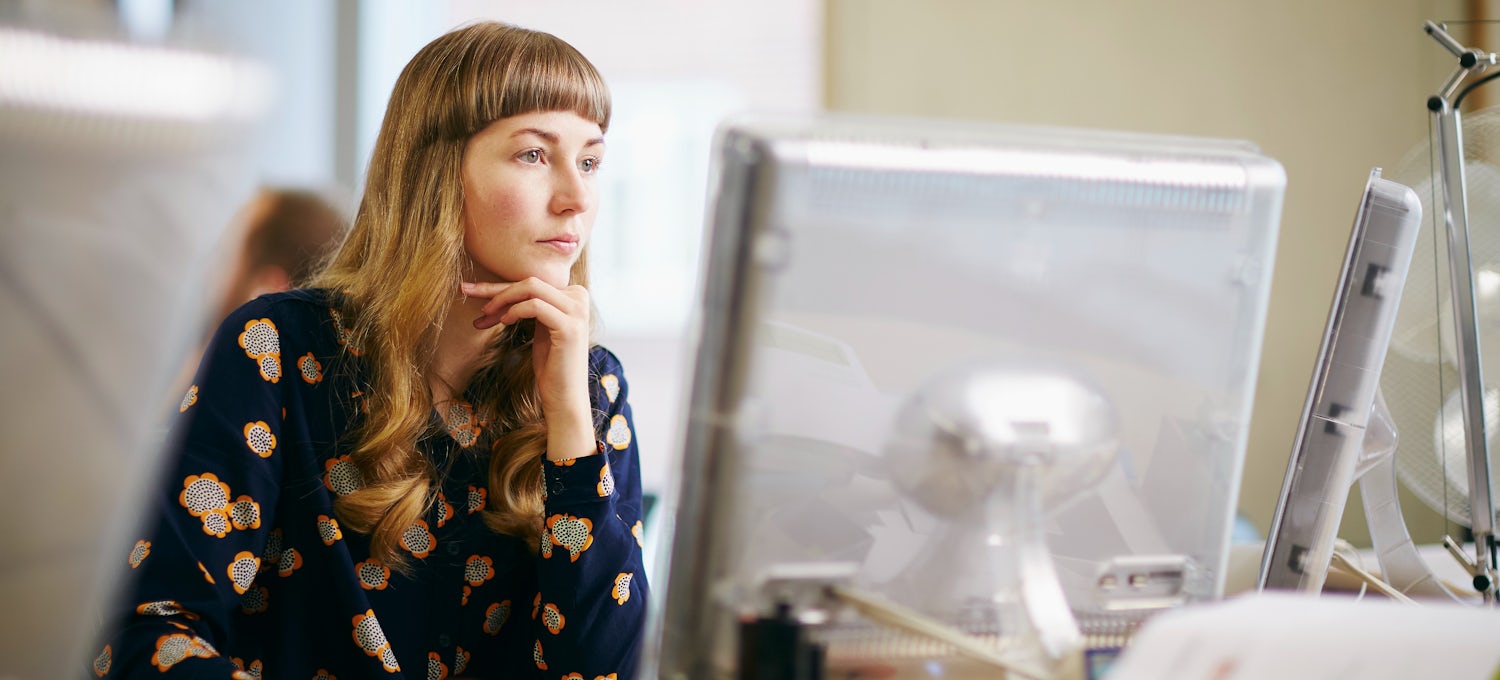 [Imagen destacada] Una persona con una blusa de flores se sienta en un escritorio y estudia para obtener un certificado de Linux en dos monitores de ordenador.