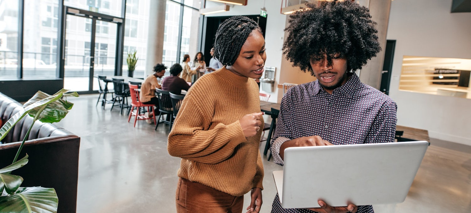 [Featured Image] Two coworkers review information on a laptop in an office.