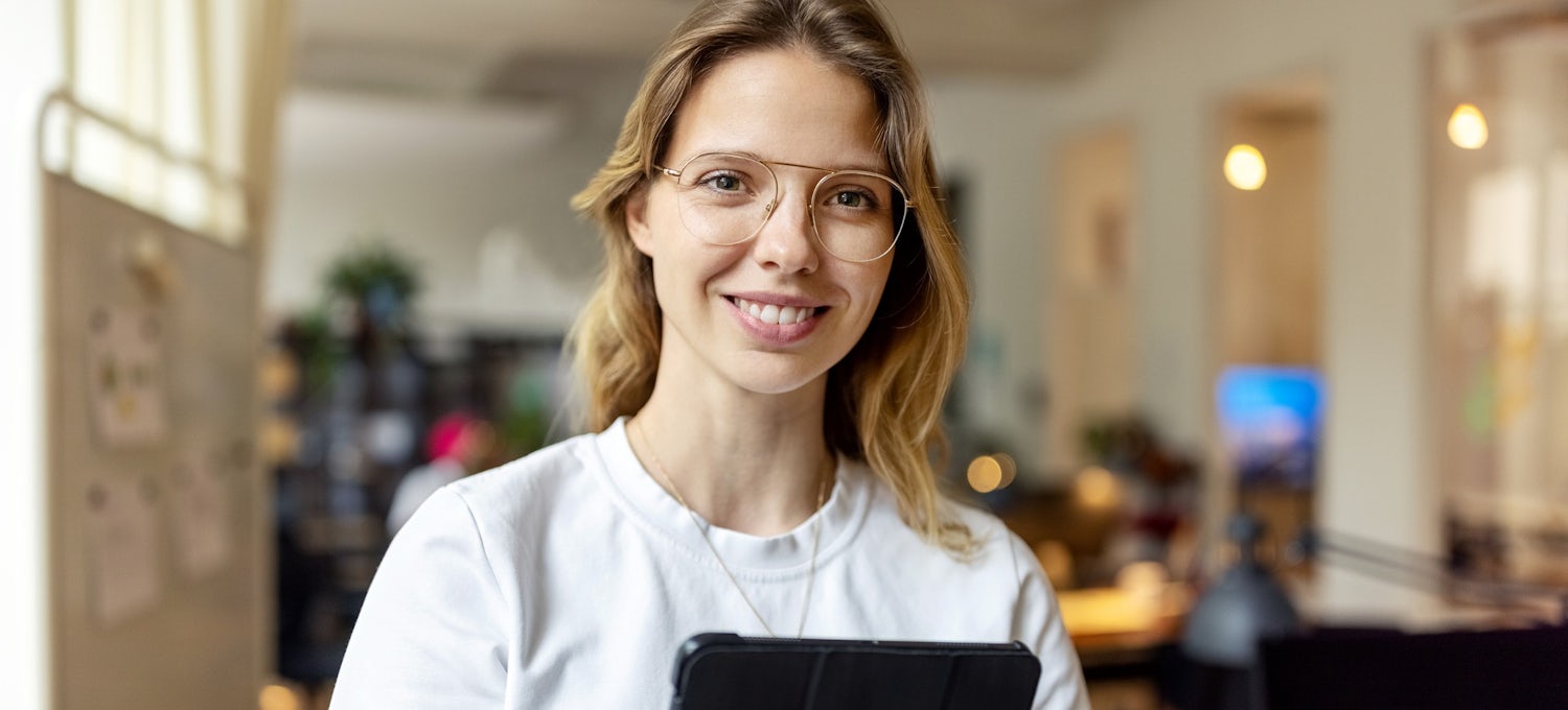 [Featured image] An Azure-certified professional stands in an office holding a tablet while smiling. 