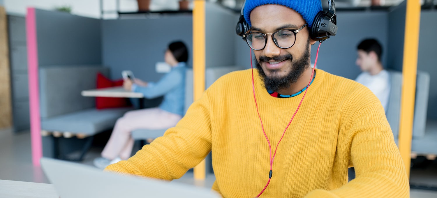 [Featured Image] A man in a yellow sweater types on a laptop in a co-working space.