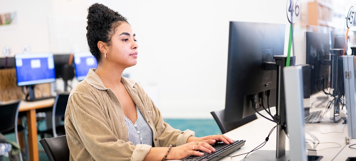 [Featured Image] An employee sits at a computer and uses the activation function in a neural network to solve complex problems. 