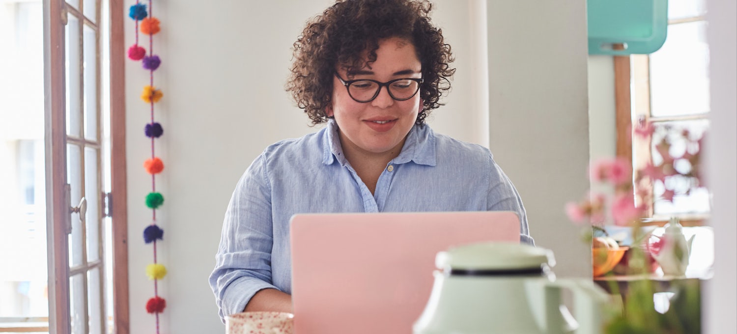 [Featured image] A person with curly hair and glasses works on a resume on a pink laptop computer.
