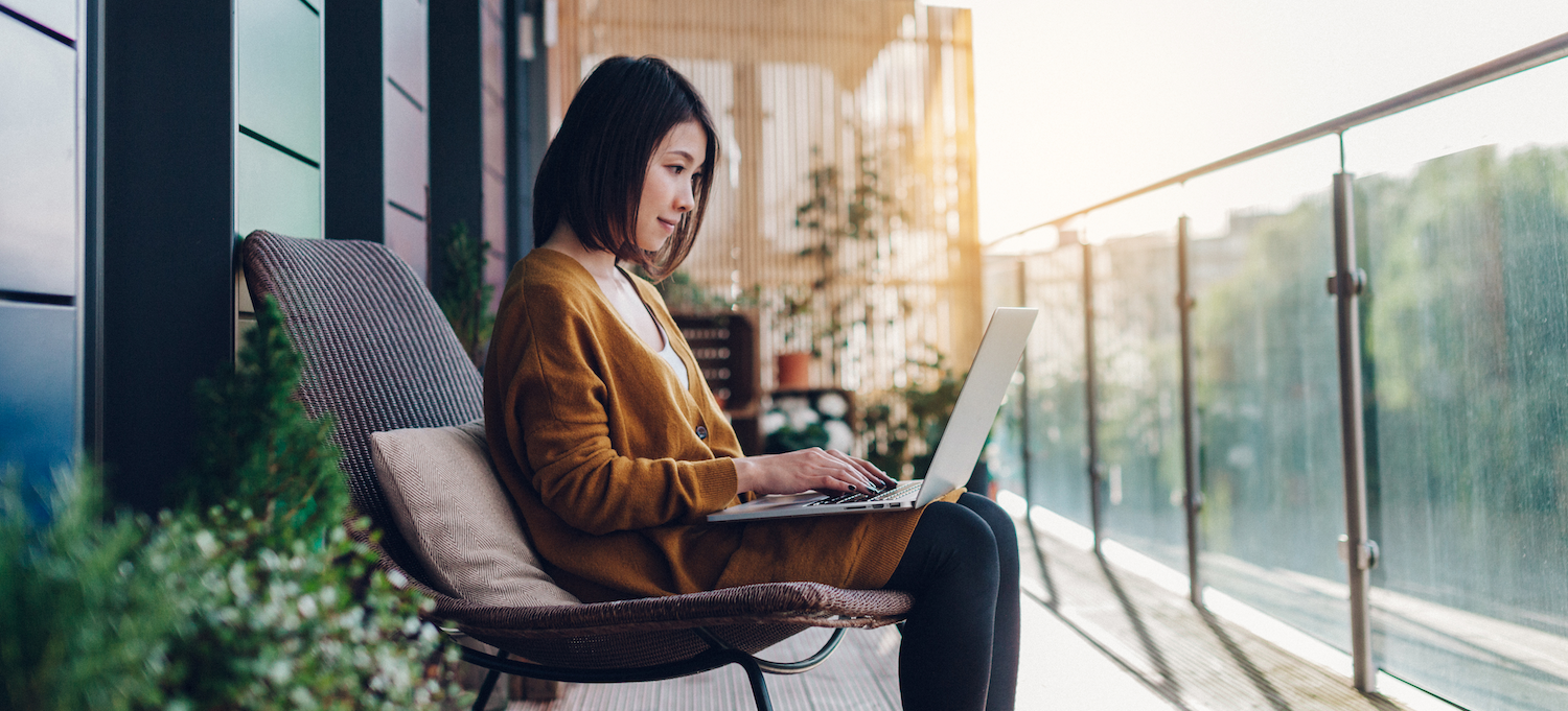 [Image en vedette] Une femme assise sur une terrasse extérieure avec son ordinateur portable sur ses genoux travaille sur son portfolio