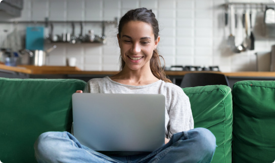 A woman sitting on a green couch with a laptop open