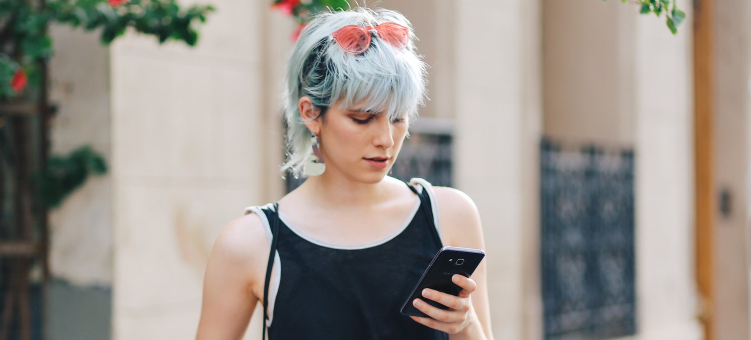 [Featured image] A young woman with light blue hair checks her phone.