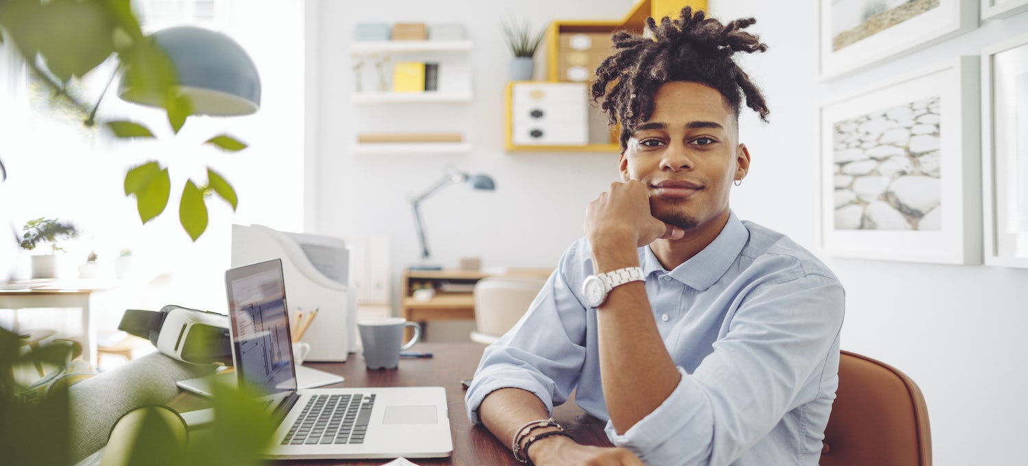 [Featured image] A young Black man with dreads sits in front of his laptop smiling.
