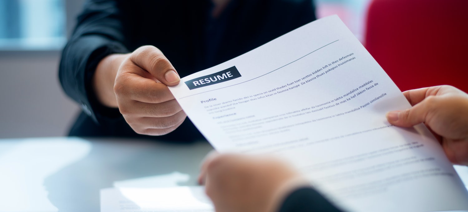 [Featured Image] Close-up view of a printed resume being handed to an interviewer.