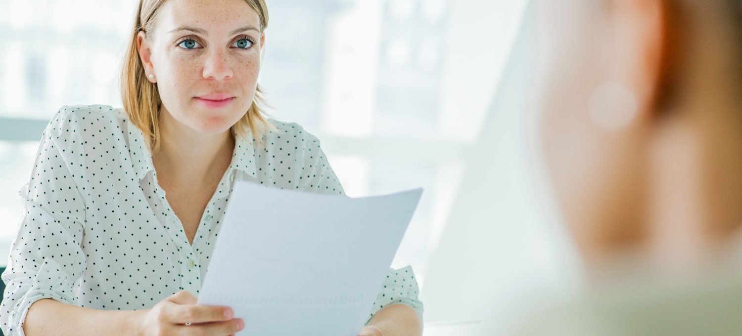 [Featured Image] A woman interviews at an office and holds her CV, which contains a supporting statement.