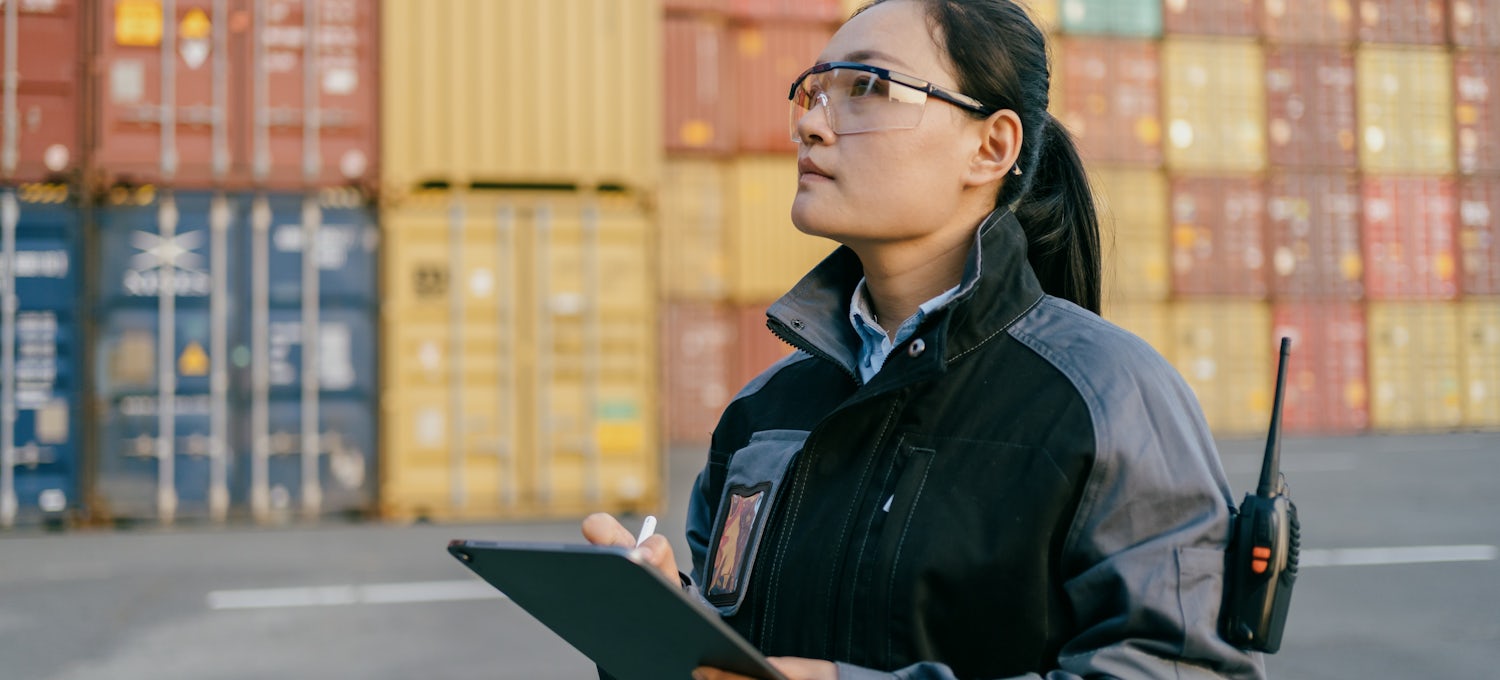 [Featured Image] A logistics specialist checks her tablet at a container terminal.