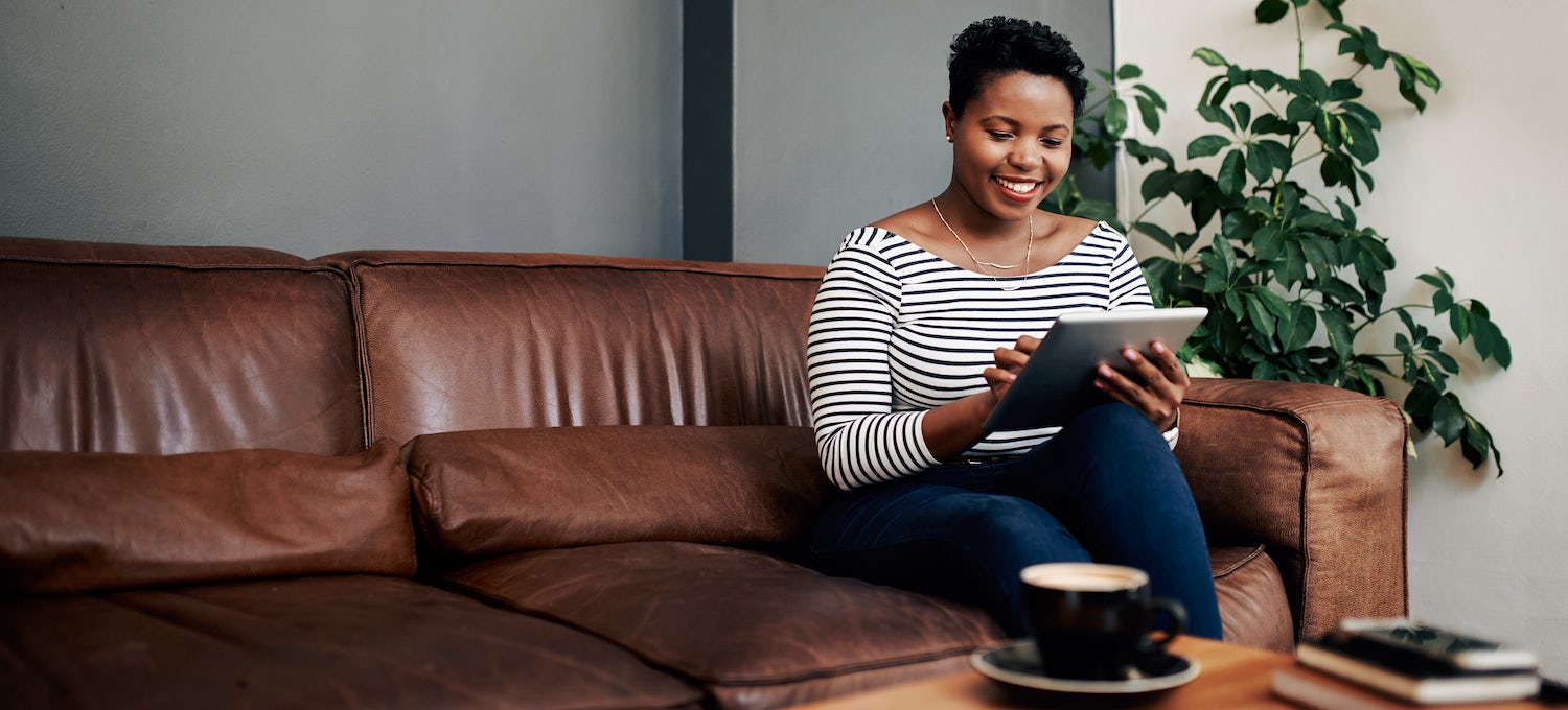 [Featured image] A Black woman in a striped top sits on a leather couch and completes her FAFSA on a tablet. 