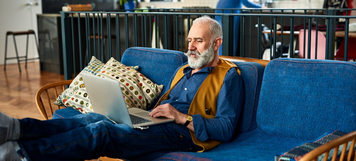 [Featured image] An older man wearing a vest does affiliate marketing on his laptop as he reclines on a couch at home. 