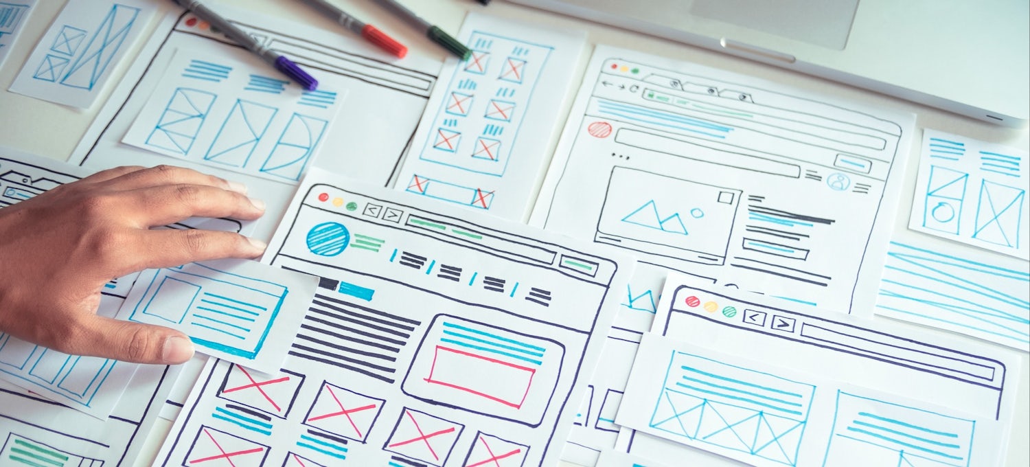 [Featured Image] A visual designer looks over sketches and drawings of a website or application design.
