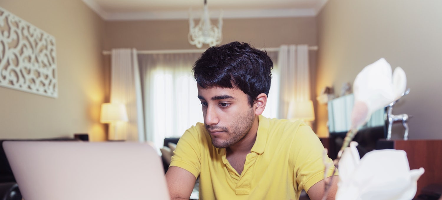 [Featured Image] A product manager in a yellow polo shirt works from home on a silver laptop.