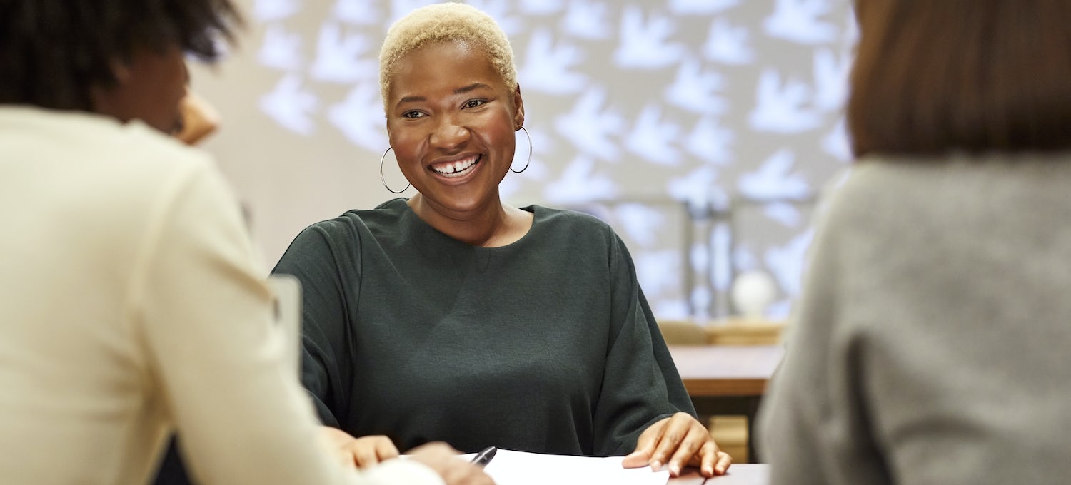A smiling woman with short hair and earrings sits at a table during a UX designer job interview