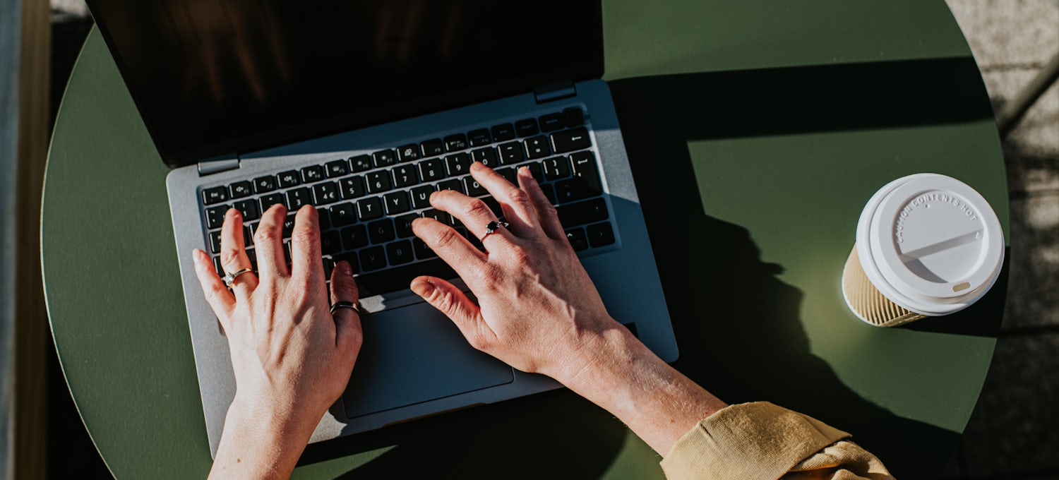 [Featured image] A pair of hands type on a laptop on a green table.