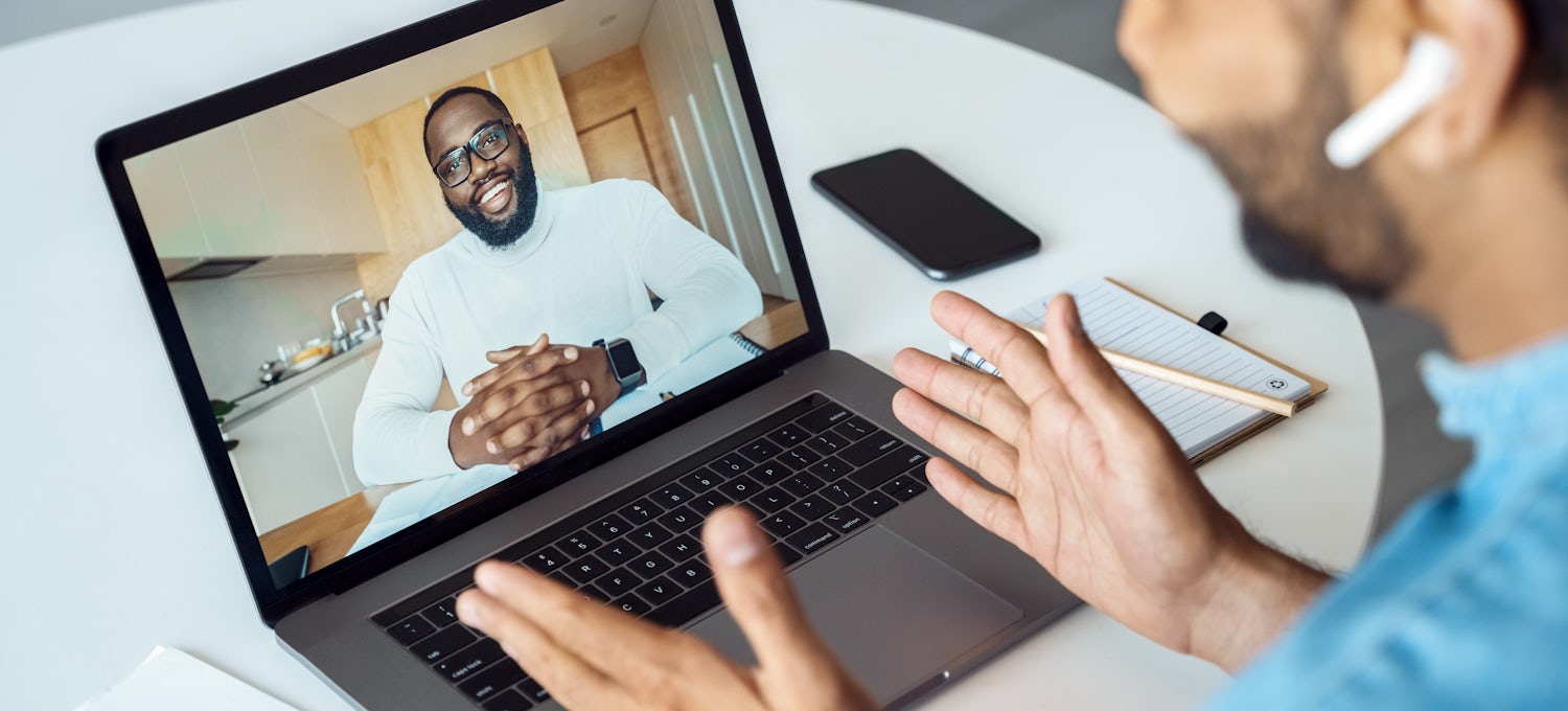 [Featured image] A person in a blue shirt and wearing AirPods uses their laptop to discuss cybersecurity interview questions on a video call. 
