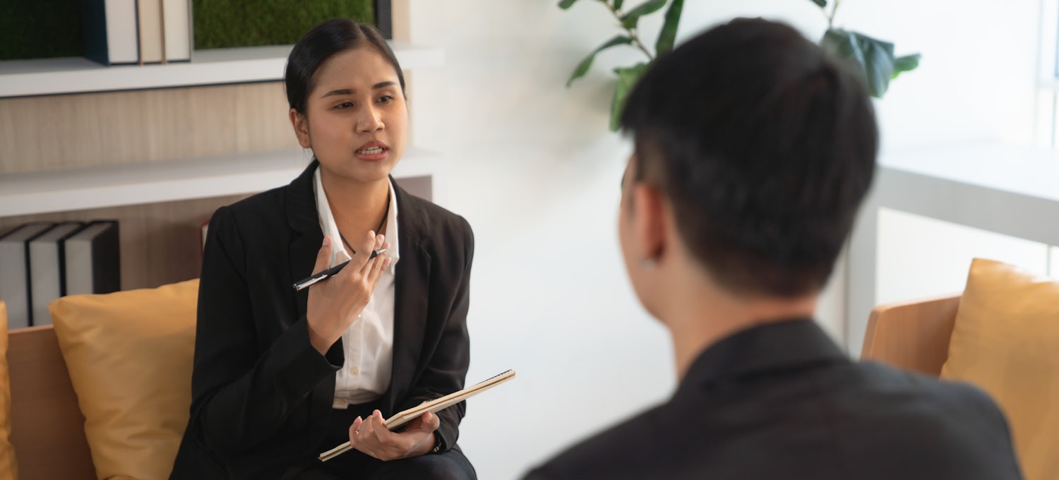[Featured image] A hiring manager in a business suit writes on a notepad as she interviews someone for a leadership role.