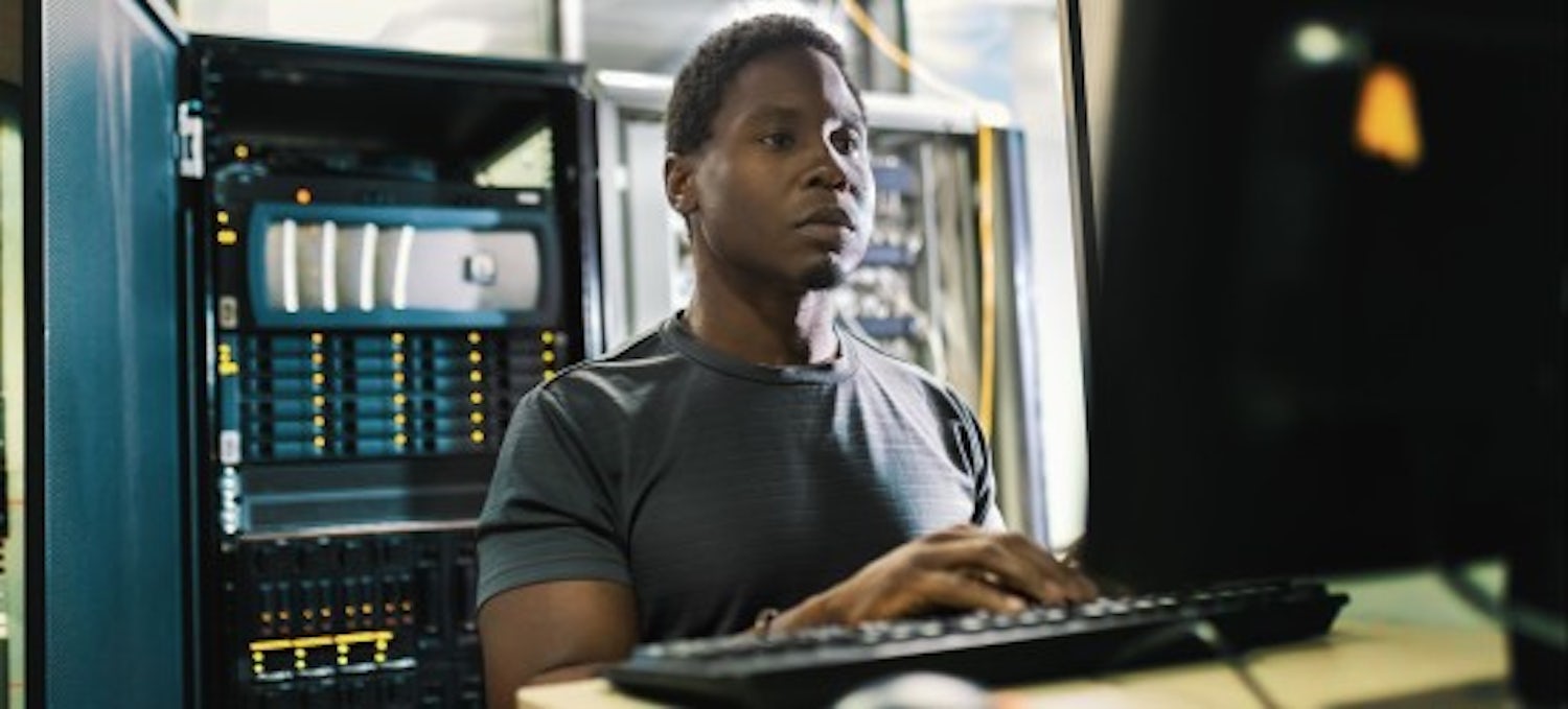 [Imagen destacada] Un empleado de informática forense en una estación de trabajo con un servidor detrás.