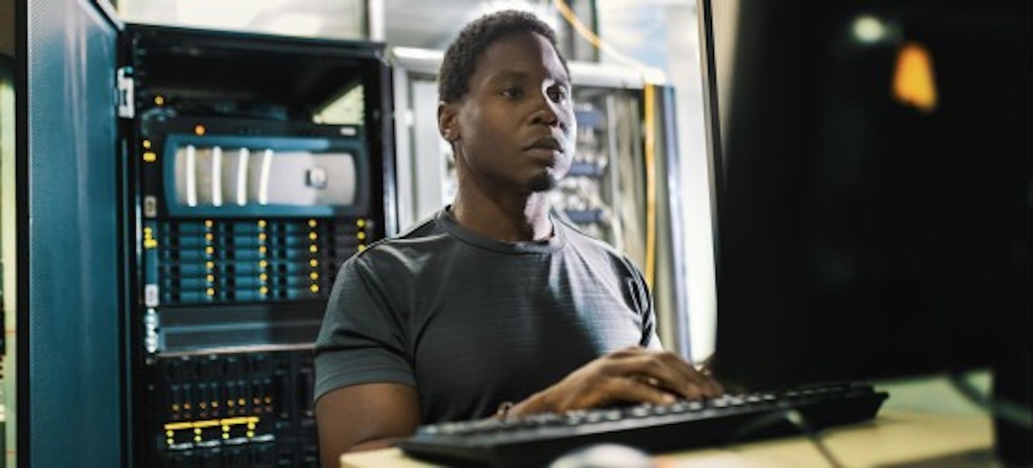 [Imagen destacada] Un empleado de informática forense en una estación de trabajo con un servidor detrás.