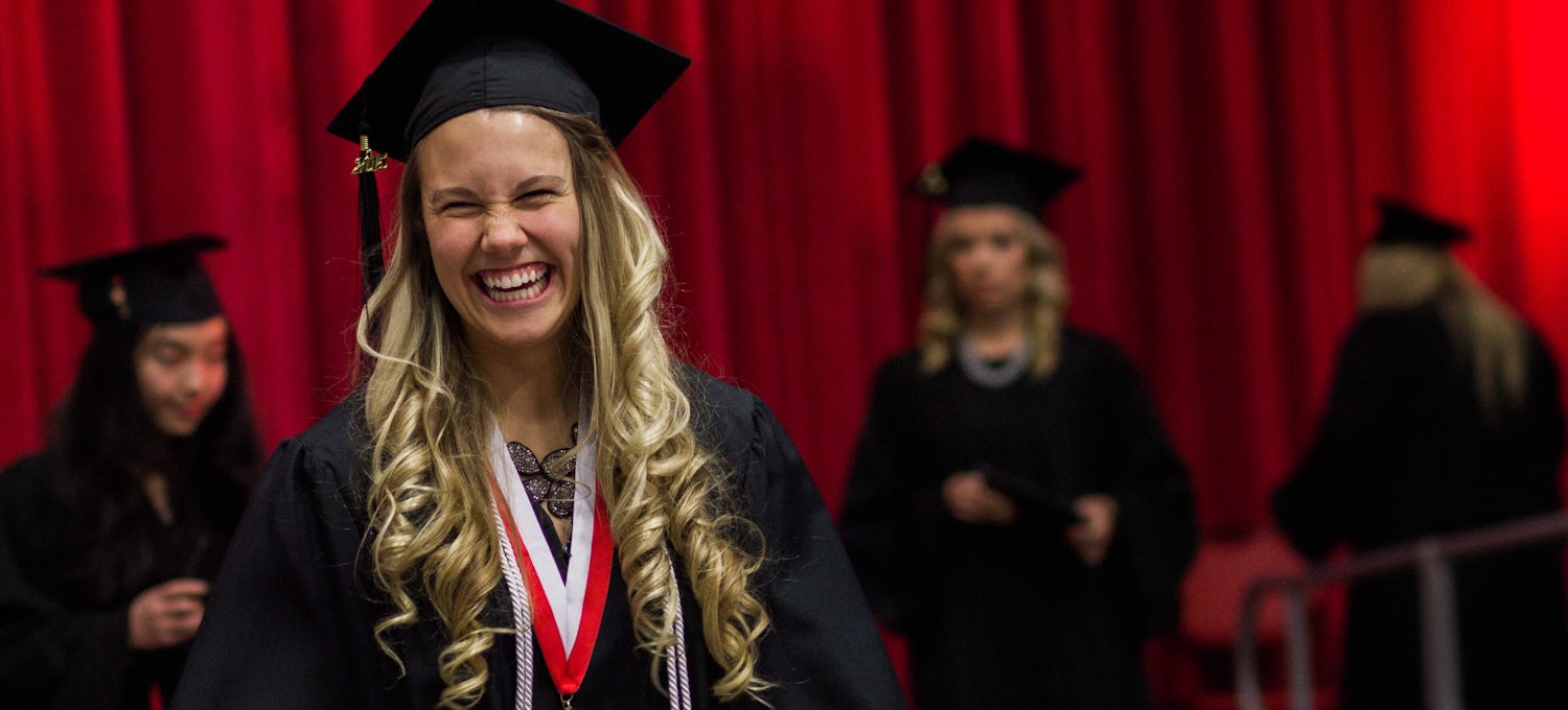 [Featured image] A baccalaureate student in a cap and gown smiles on stage after getting her degree.