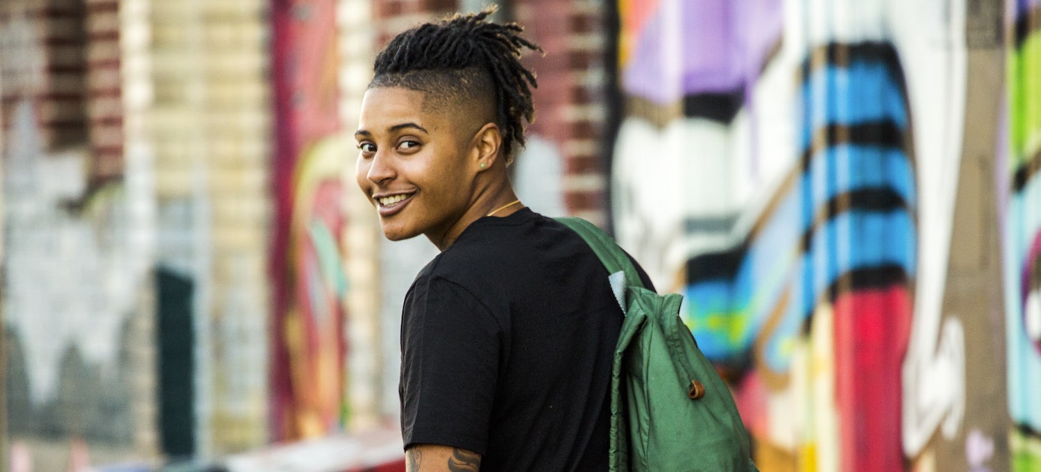 [Featured image] A passive income business owner wearing a black t-shirt and green backpack turns around and smiles at the camera while walking by colorful buildings.