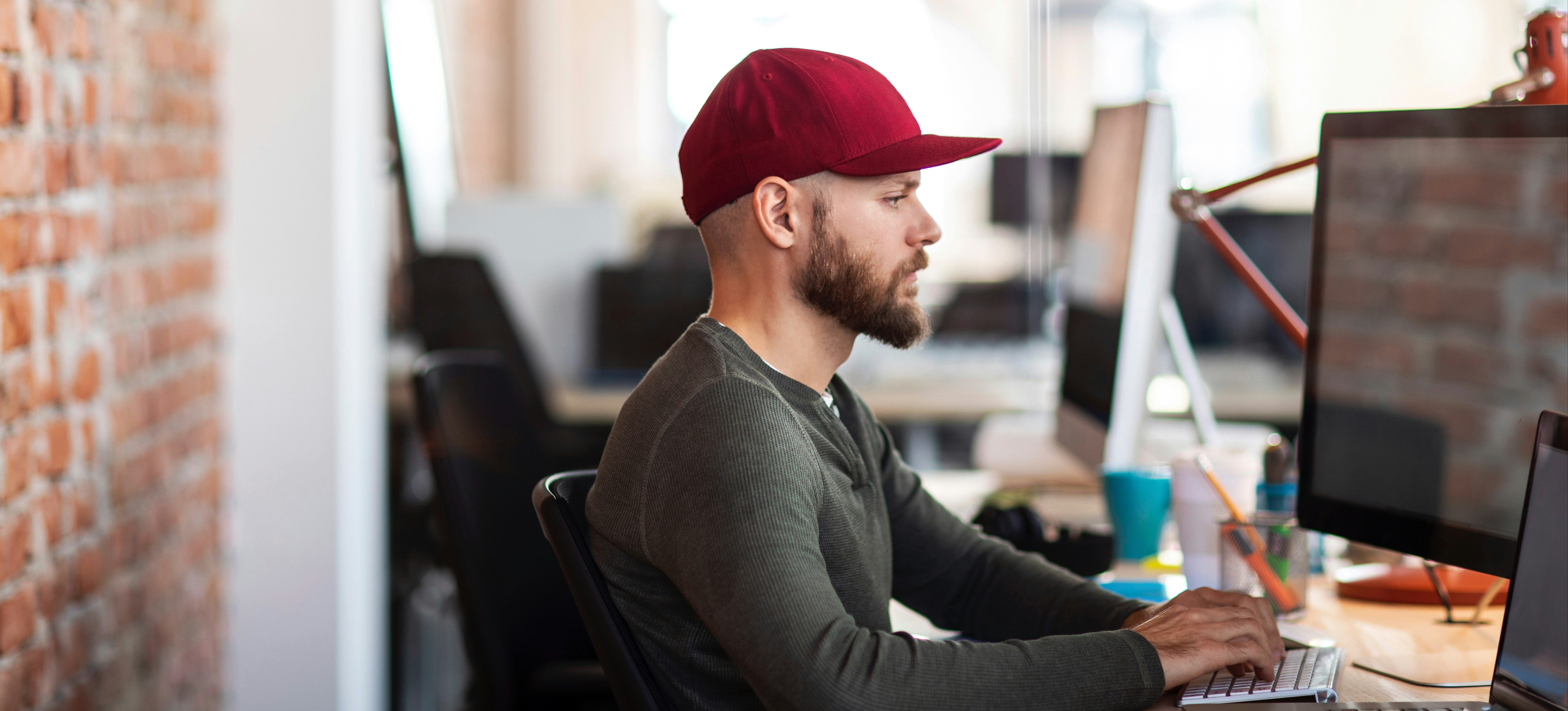 [Featured Image]: An NFT developer in a red ballcap focuses intently on their computer screen as they work on their current project. 
