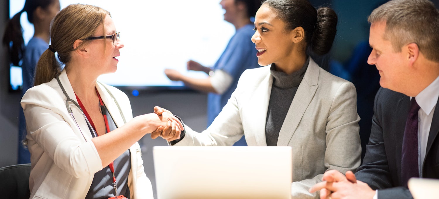 [Featured Image] A professional meets and shakes hands with potential customers as part of her cybersecurity sales job.