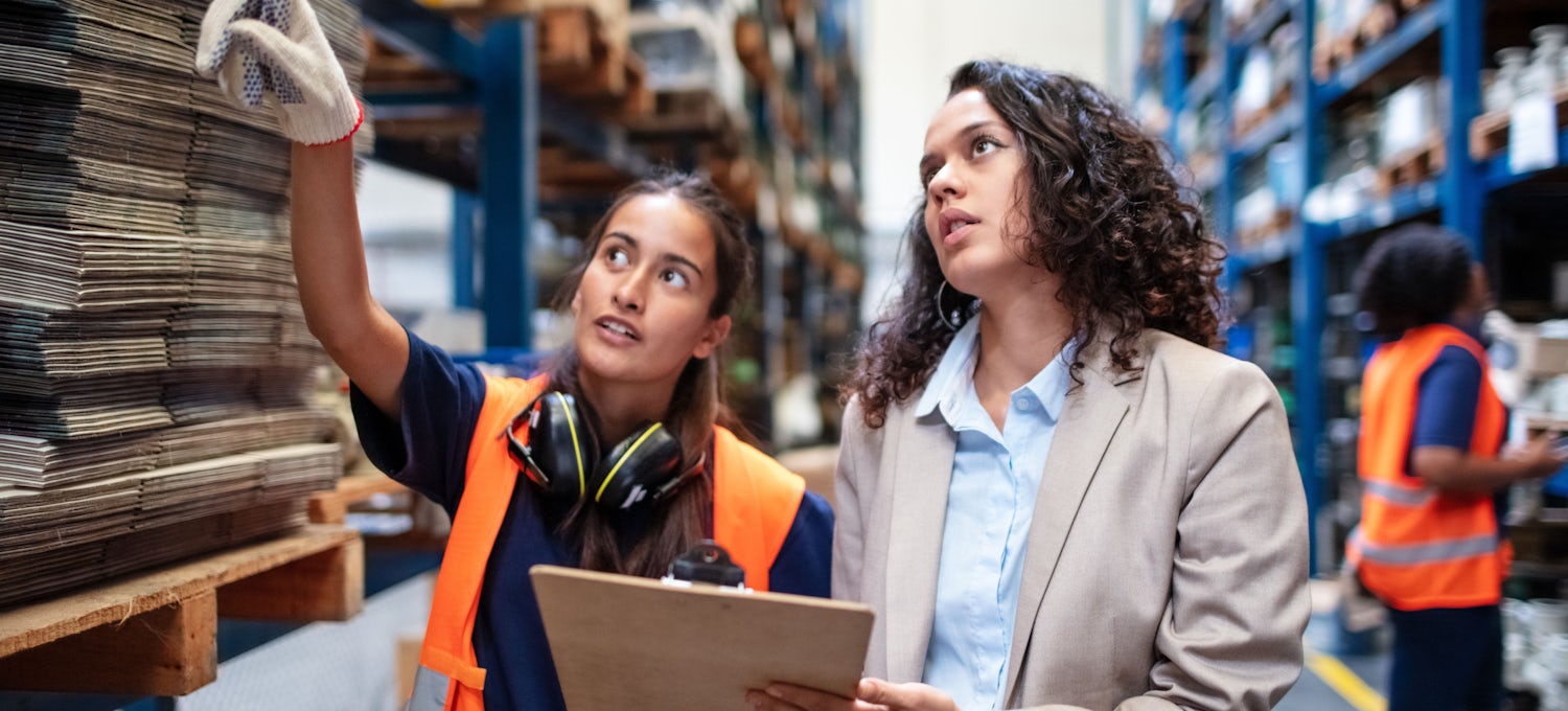 [Featured Image] Two women are at a material supplier discussing what they need, one person is holding a clipboard while the other is pointing to materials. 