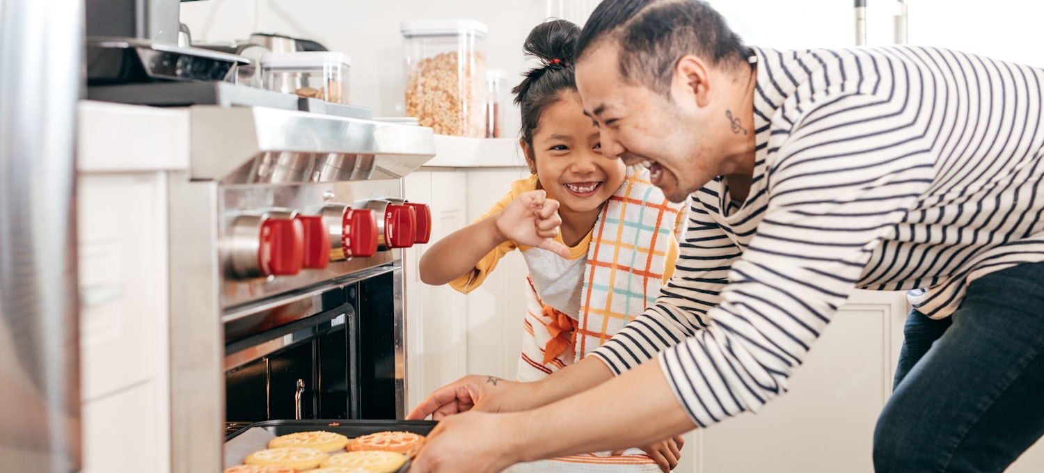 [Featured image] Side hustler pulling cookies out of an oven with a child standing next to him making him laugh.