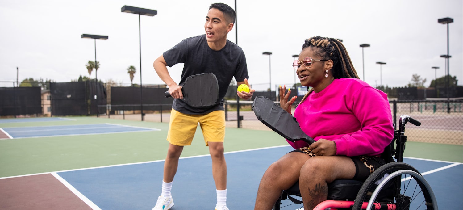 [Featured image] An exercise physiologist plays tennis with a client in a wheelchair.