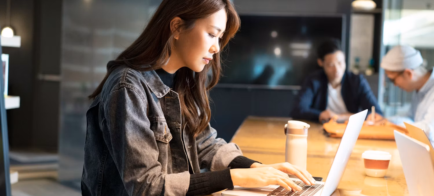 A person sitting in a cafe, looking up IT certifications on their laptop.