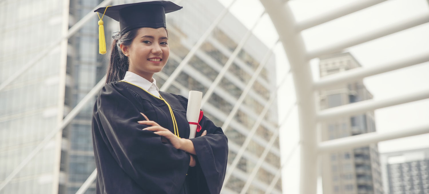 [Imagen destacada] Una joven con toga y birrete sostiene su diploma y sonríe. 